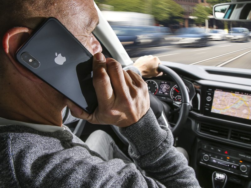 Mann telefoniert am Steuer eines Autos während der Fahrt mit Smartphone am Ohr.